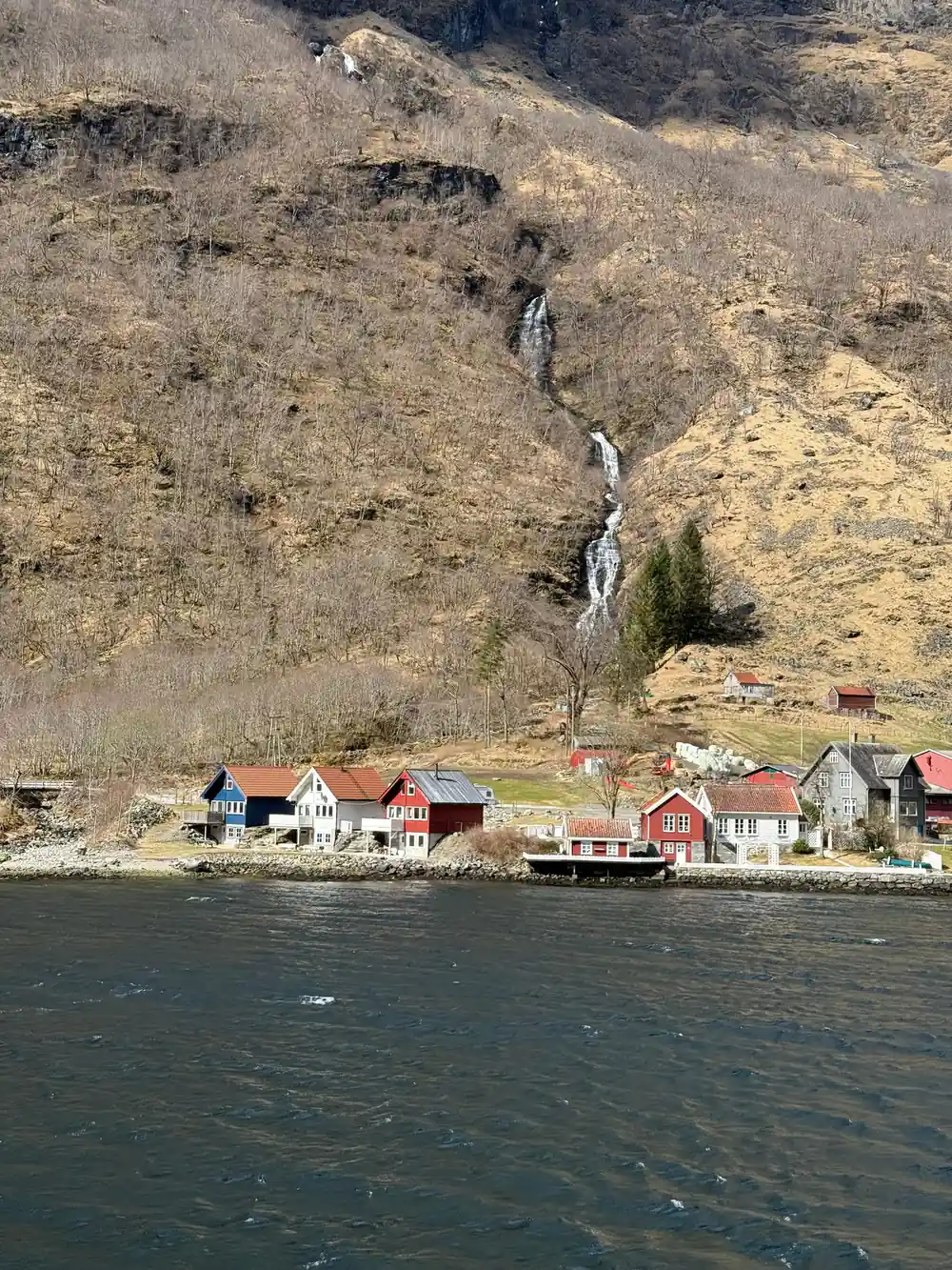 A cluster of red and white houses on the shore below a waterfall