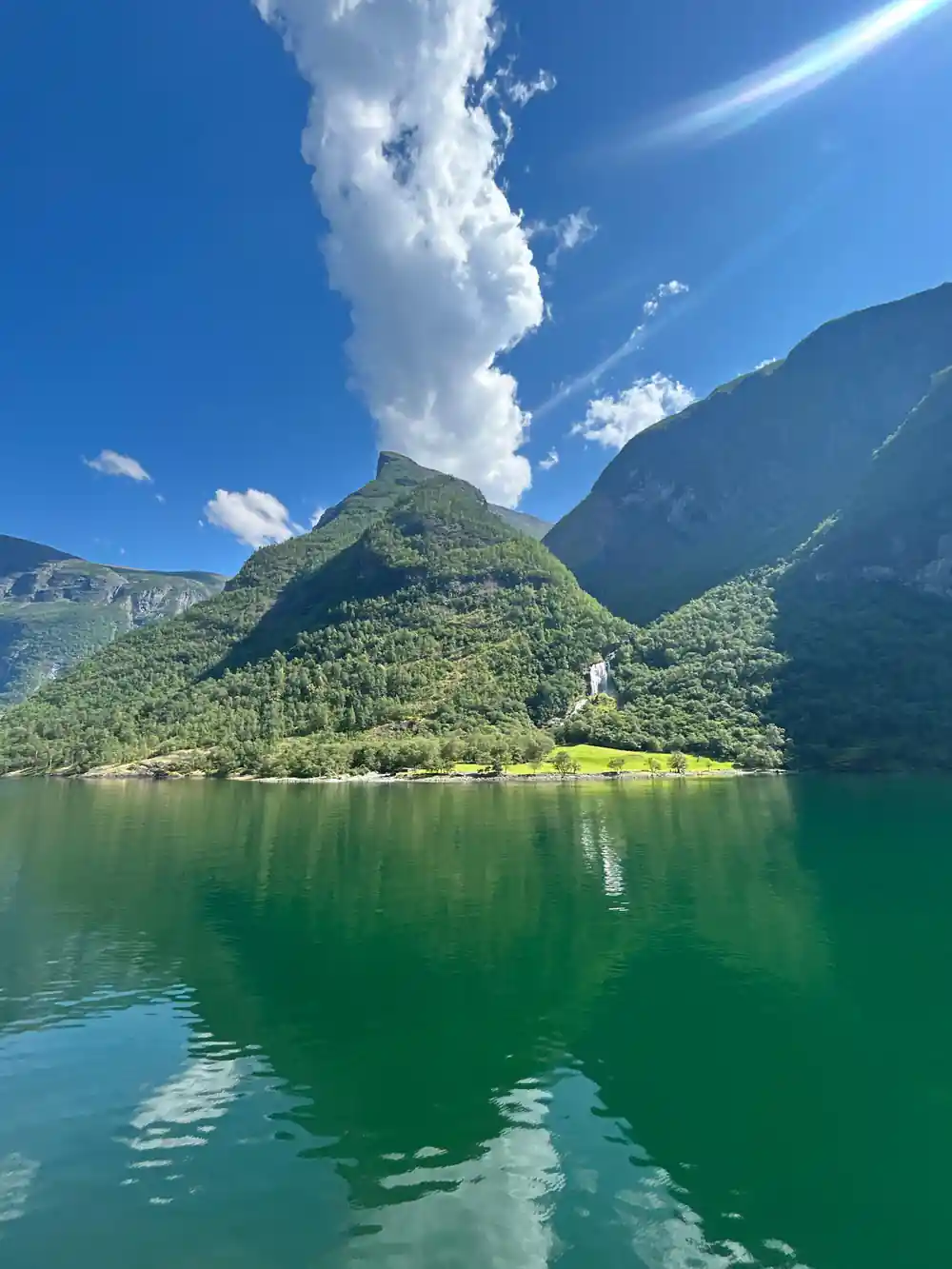 A green headland dividing the fjord, reflected in flat water