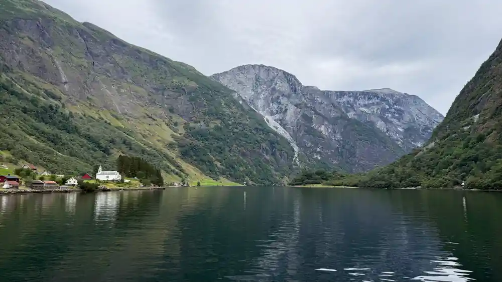 A grey rock face rising straight out of calm green water