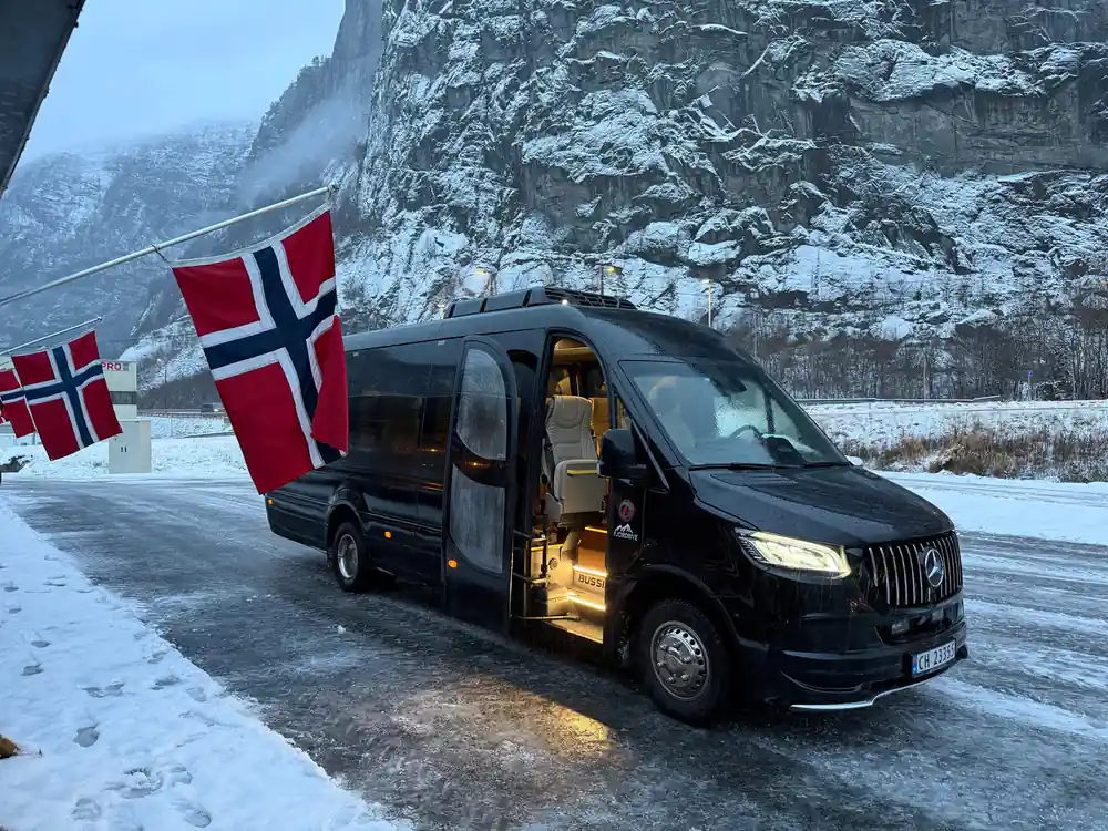 The operator's black minibus with a Norwegian flag on a snowy road