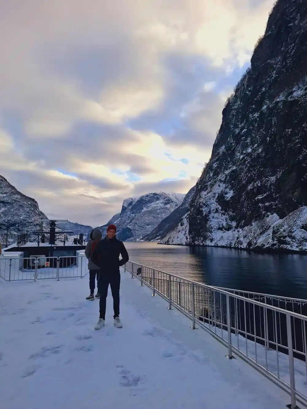 A passenger on the snow-covered deck as the boat runs down the fjord