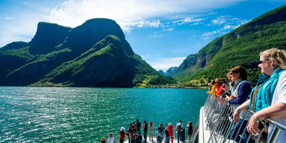 Passengers along the bow rail of the fjord boat between green walls