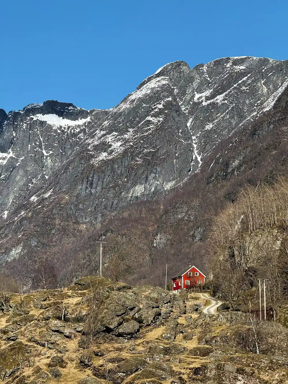 A single red house on the shore beneath a huge grey rock wall