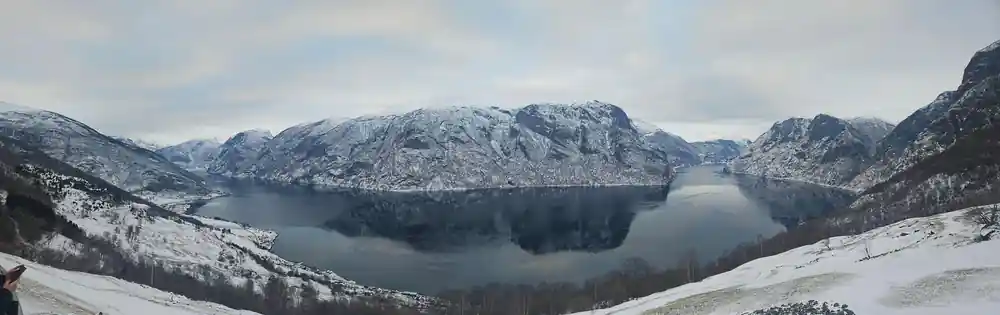 A snow-covered plateau wall mirrored in the fjord below it