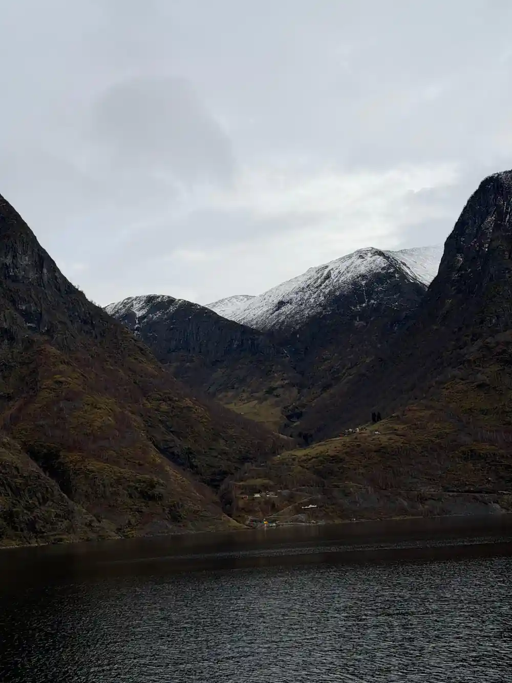 A snow-dusted mountain wall above the fjord in flat light