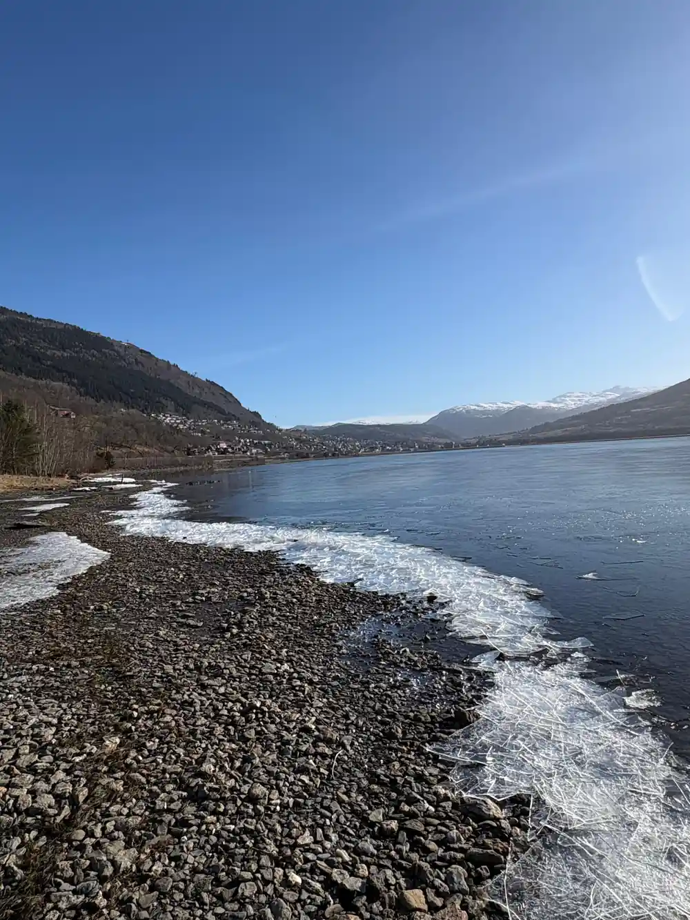 A stony shore at the head of the fjord under a clear sky